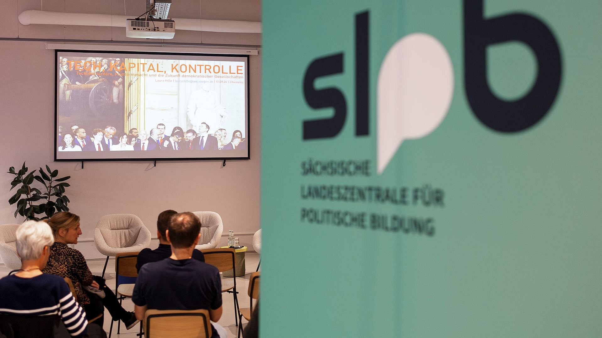 Blick in den Veranstaltungsraum mit sitzendem Publikum, einer Präsentationsfolie zum Thema „Tech, Kapital, Kontrolle“ und dem Logo der Sächsischen Landeszentrale für politische Bildung im Vordergrund.