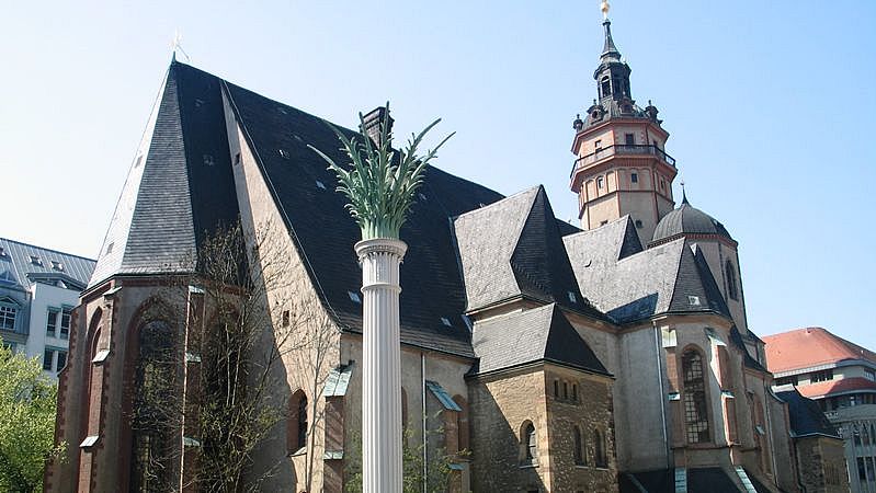 Nikolaikirche Leipzig mit Nikolaisäule, die als Friedenssäule an die Montagsdemonstrationen und die Friedhaftigkeit der Revolution erinnern soll, Foto: Dirk Goldhahn/ Gancho, Wikimedia Commons Verlinkung zu Montags- und Massendemonstrationen